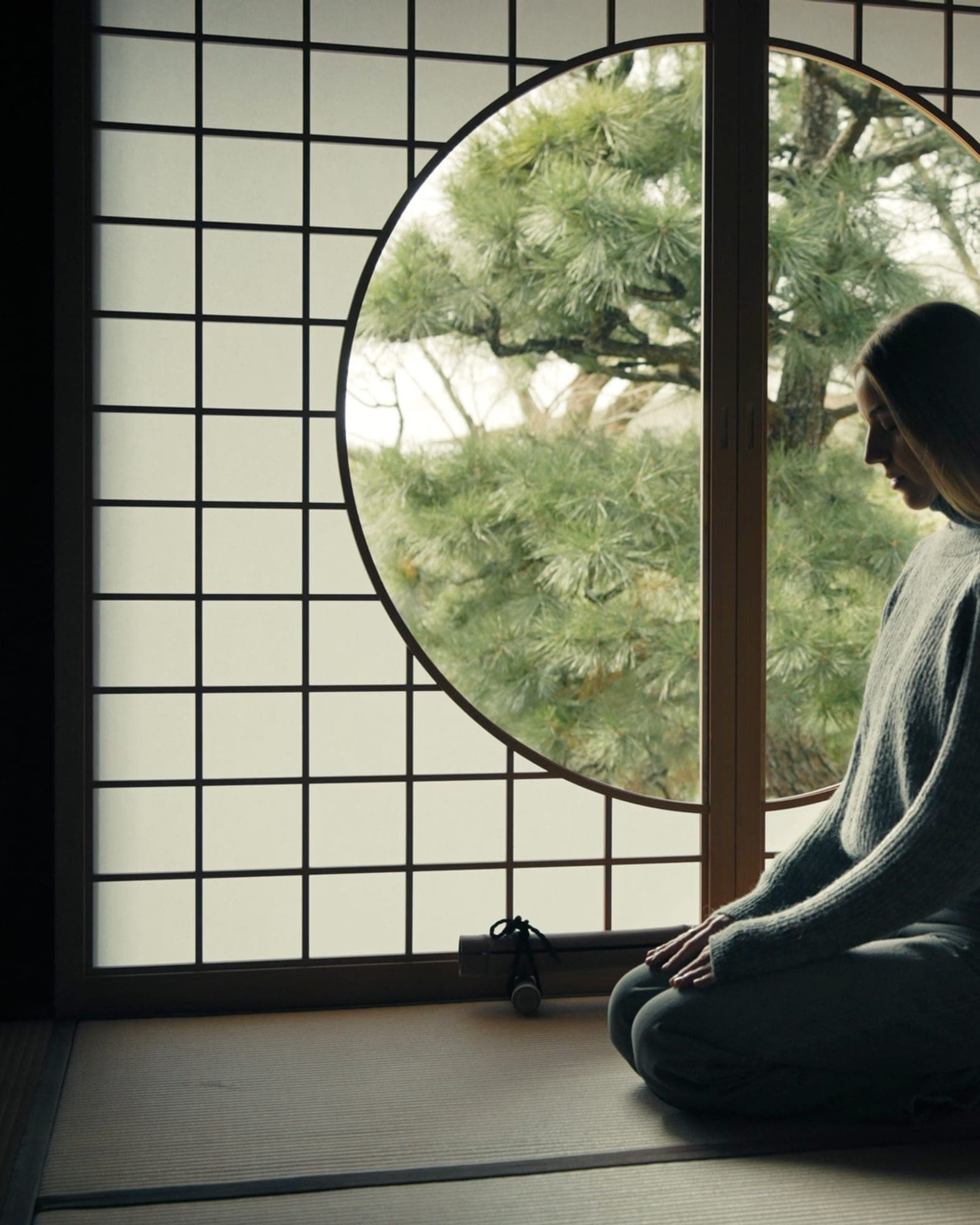 靜坐者側影,面向日式圓窗外的松——身體先安靜下來,意識才抵達。